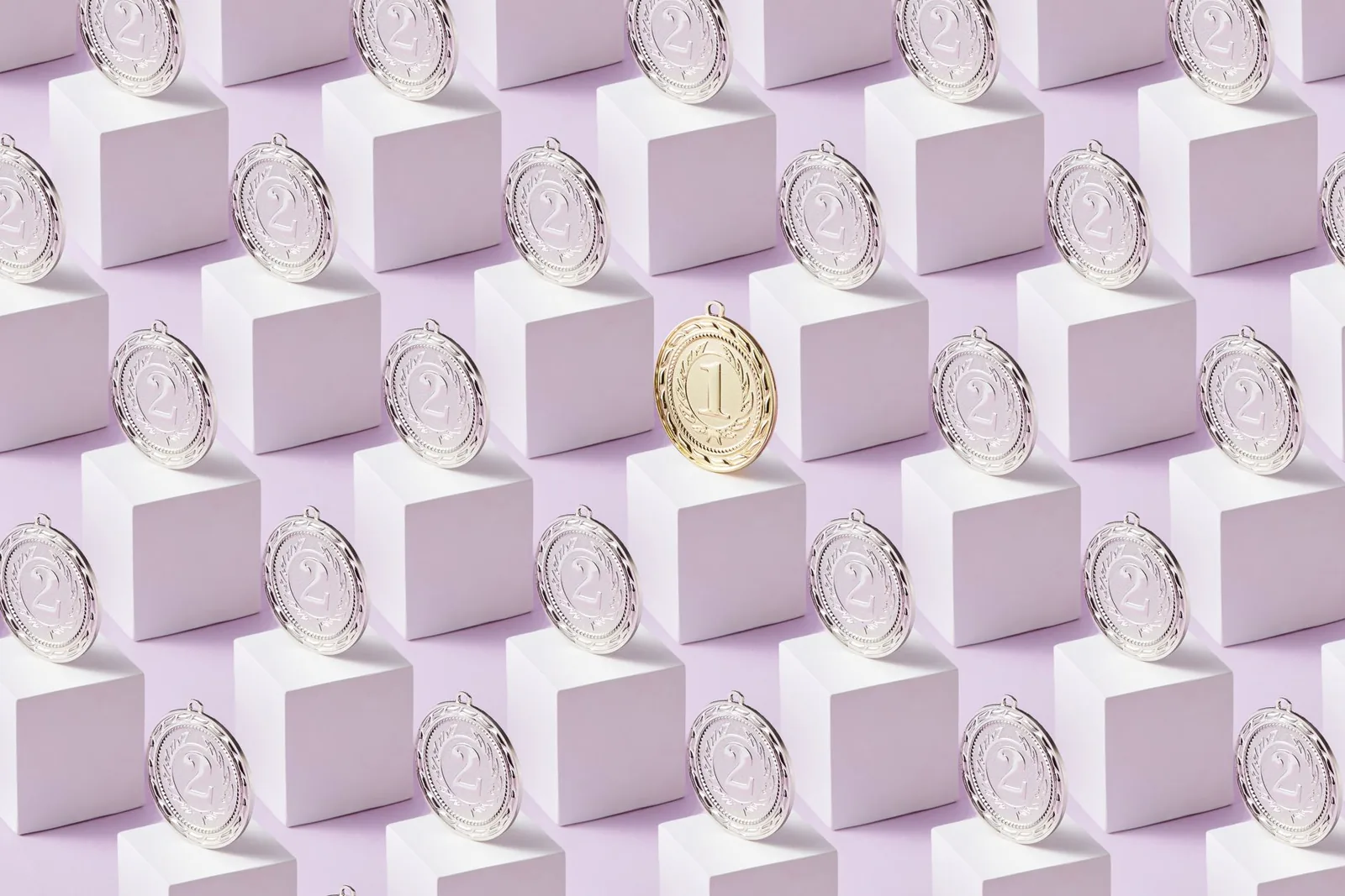 A single gold medal standing among rows of silver medals on white cubes against a pale background